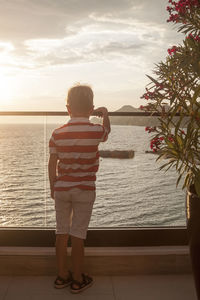 Rear view of boy standing by sea against sky