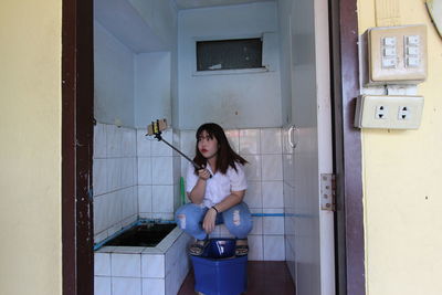 Young woman taking selfie on toilet bowl in bathroom at home