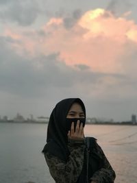 Portrait of woman standing by sea against sky during sunset