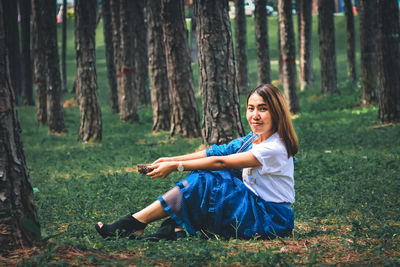 Portrait of smiling young woman sitting on tree trunk in forest