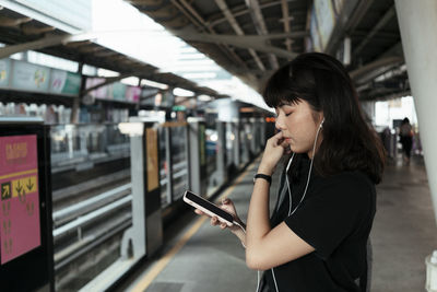 Young woman using mobile phone at railroad station