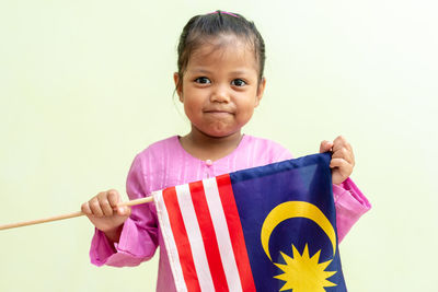 Portrait of cute girl holding malaysian flag against wall