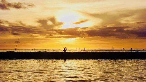 Silhouette people on sea against sky during sunset