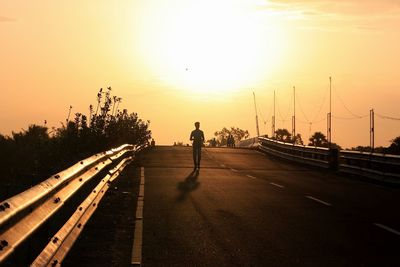 Silhouette man walking on road against orange sky during sunset