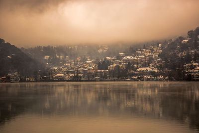 Scenic view of lake by buildings against sky during sunset