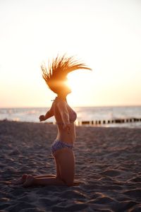 Woman standing at beach against sky during sunset