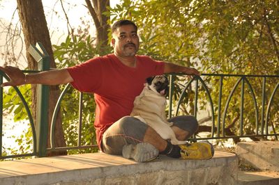 Man with dog sitting against trees