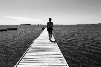 Rear view of man walking on pier over sea against sky