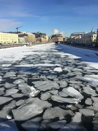 View of frozen river in city against sky