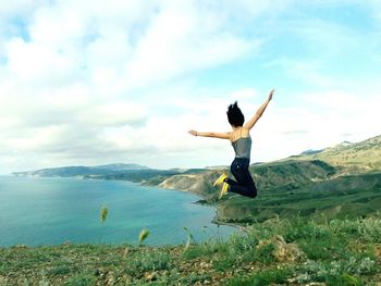 Woman with arms raised in sea against sky