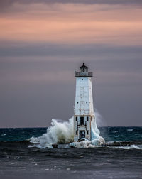 Lighthouse by sea against sky during sunset