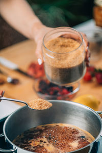 Woman cooking fruits and making homemade jam. putting brown sugar in the pot.