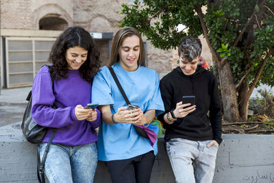 Friends using mobile phone while standing outdoors on the street.