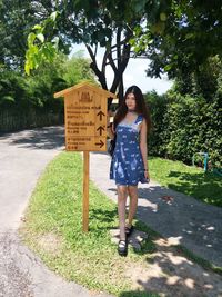 Portrait of woman standing by information sign on footpath