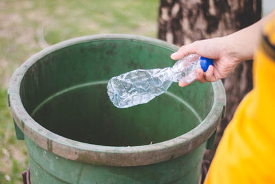 Cropped hand throwing bottle in garbage can