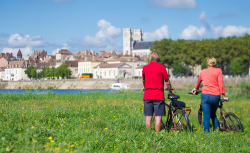 Rear view of people with bicycles on grassy field against sky