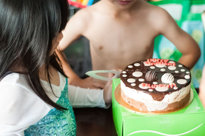 Midsection of shirtless boy cutting cake with sister