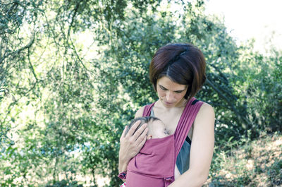 Mother carrying toddler daughter against trees