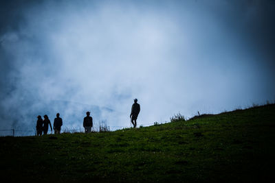 Rear view of people walking on field against sky