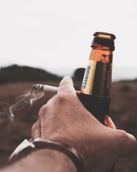 Close-up of hand holding cigarette against sky