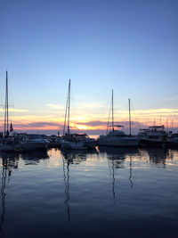 Sailboats moored in harbor at sunset