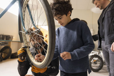 Boy learning to fix valve on bicycle wheel by technician at recycling center