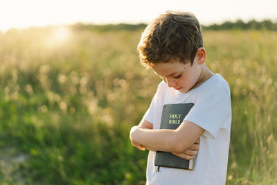 Christian boy holds bible in her hands. reading the holy bible in a field during beautiful sunset