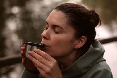 Young woman drinking tea from thermos outdoors