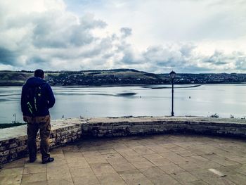 Rear view of man looking at lake against sky