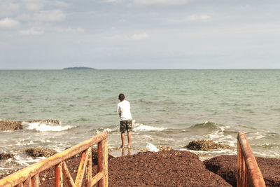 Rear view of man fishing at beach against sky