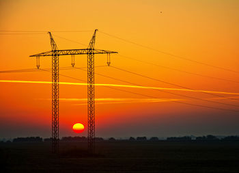 Silhouette electricity pylon on field against romantic sky at sunset