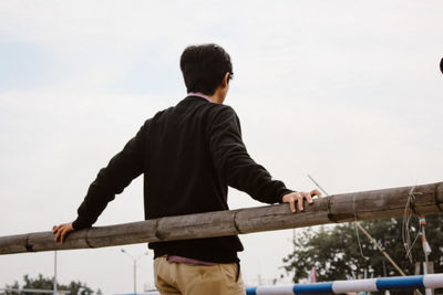 Rear view of boy standing by railing against sky