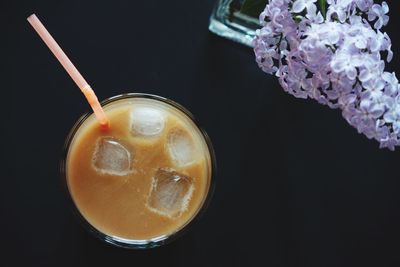 Directly above shot of iced coffee with purple flowers against black background