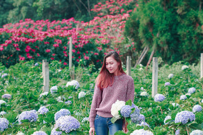 Portrait of smiling woman standing by flowering plants