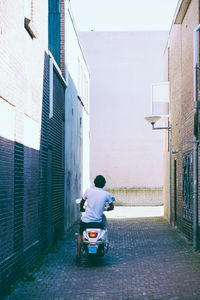 Rear view of people riding motorcycle on street amidst buildings