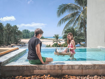 Woman sitting by swimming pool against sky