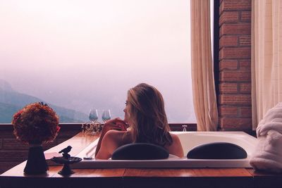 Rear view of naked woman in bathtub against window