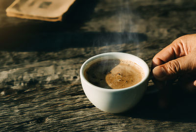 Cropped image of hand holding coffee cup on table