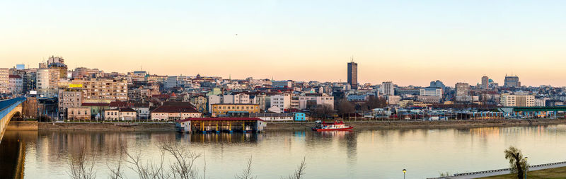 Scenic view of river by buildings against sky during sunset