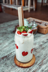 White smoothie in glass with straw, sliced strawberry on wooden table. healthy dessert for breakfast