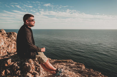 Man sitting on rock looking at sea against sky