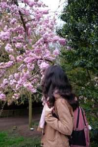 Rear view of woman standing by pink flowering tree