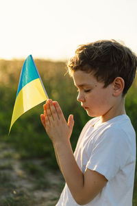 Ukrainian boy closed her eyes and praying to stop the war in ukraine in a field at sunset