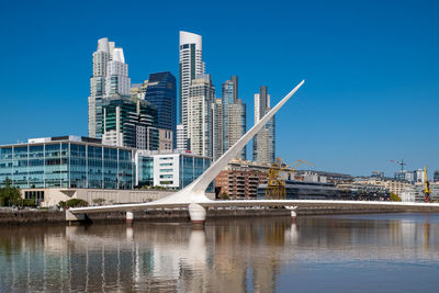 Bridge over river by buildings against clear sky