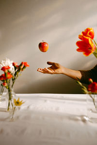 Crop anonymous person tossing ripe apple in air above table with tulips and fresh carnations person