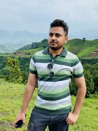 Portrait of young man standing on field against sky