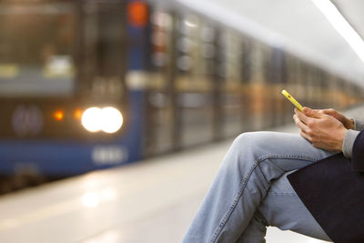 Midsection of man using phone at railroad station