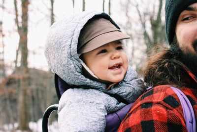 Smiling father carrying daughter in baby carrier against trees