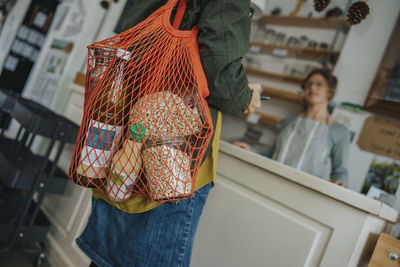 Female customer carrying mesh bag full of groceries in retail store