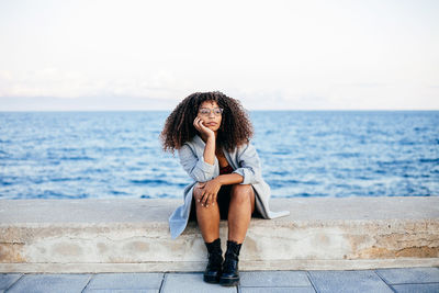 Young woman sitting on beach against sky